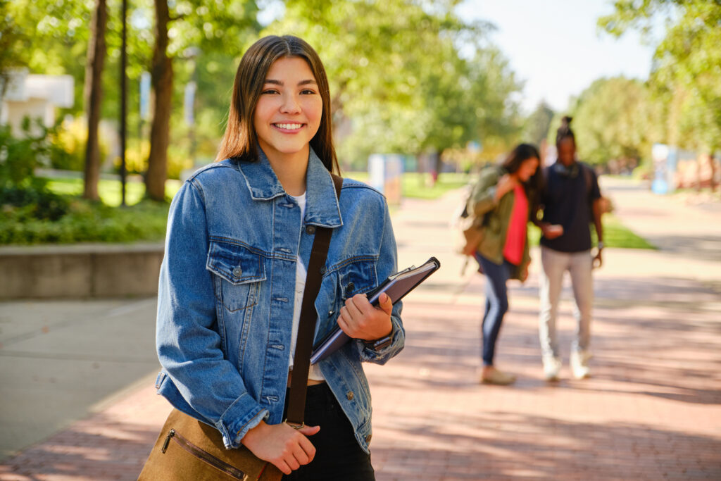 trade school student standing on campus wtih books smiling at the camera