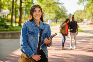 trade school student standing on campus wtih books smiling at the camera